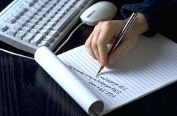 Picture of person's hand writing with pen beside computer keyboard, editing, proofreading, writing